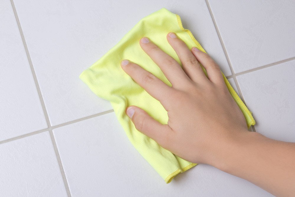 Wiping white floor tile with a yellow microfibre cloth