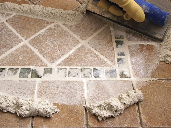 Applying new grout between beige floor tiles